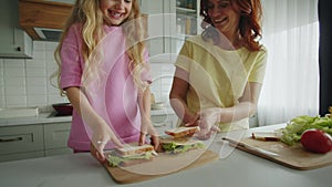 Friendly and smiling mother with daughter in the kitchen are folding sandwiches and hugging warmly. Showing a high five