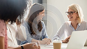 Friendly smiling old and young businesswomen talking laughing at meeting