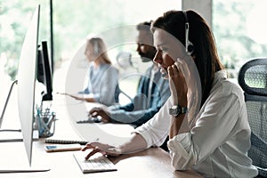 Friendly smiling woman call center operator with headset using computer at office.