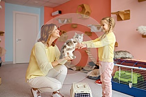 Friendly smiling woman giving cat to little girl over animal shelter background