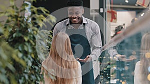 Friendly smiling young male waiter in apron serves client girl in cafe affable restaurant worker barman brings coffee