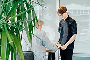 Friendly smiling young male waiter serves a client in cafe. Affable restaurant worker brings coffee drink. Man in