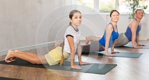 Friendly sporty parents with tween daughter and son performing Cobra Pose or Bhujangasana on gymnastic mats barefoot in