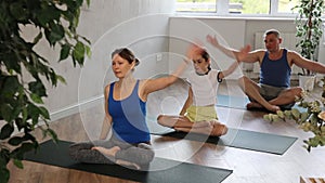 Friendly sporty parents with tween daughter and son stretching to sides while sitting in Lotus pose on mats in yoga
