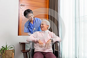 Friendly staff caregiver of nursing home talking to asian senior man in living room
