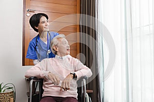 Friendly staff caregiver of nursing home talking to asian senior man in living room