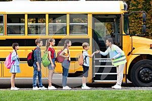 Friendly teacher lady fist bumping with kids as they boarding school bus