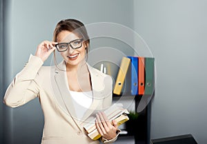 Friendly teacher, psychologist, librarian, or business coach. Beautiful smiling woman in jacket and glasses holding a stack of