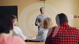 Friendly teacher is talking to his students checking knowledge, young man is raising hand and answering question, other