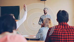Friendly teacher is talking to his students checking knowledge, young man is raising hand and answering question, other