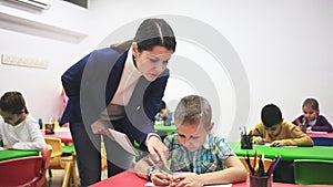 Friendly teacher woman helping children during lesson in schoolroom