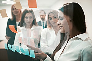 Friendly team, business people brainstorming together looking on colorful stickers on office door window indoors