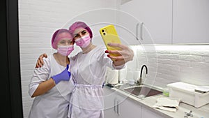 Friendly team of a dentist and assistant making selfie on mobile phone in white dentistry clinic