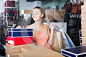 Friendly teenager female holding boxes in shoes boutique