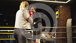 Friendly trainer teaching fit girl on boxing ring. Opponents boxing at gym