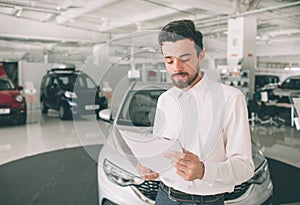 Friendly vehicle salesman presenting new cars at showroom. Photo of young male consultant showing new car in auto show