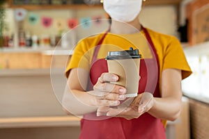 Friendly waitress woman wearing protection face mask waiting serving hot coffee cup to customer in cafe coffee shop, cafe restaura