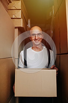 Friendly warehouse worker carrying box, standing between stacked boxes