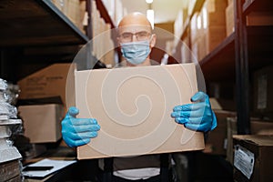 Friendly warehouse worker carrying box, wearing mask and gloves. Selective focus