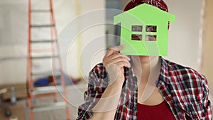 Friendly woman holds a symbol of aeco-friendly house in front of her face
