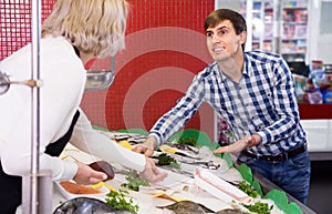 Friendly woman selling fish to male customer in store