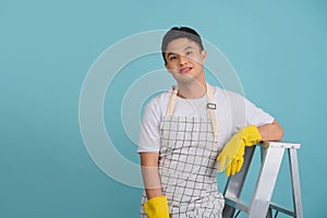 Friendly young Asian male repairman sitting on the stairs isolated on light blue background