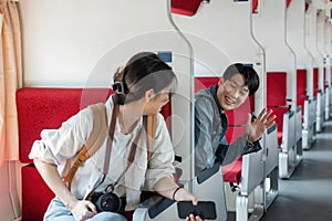 friendly and young Asian male traveler waves his hand, greeting a new friend during the trip on a train. Friendship and