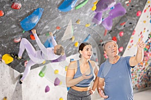 Friendly young female coach of climbing gym instructing aged man