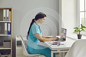 Friendly young female doctor in a blue medical suit with a stethoscope gives an online consultation.