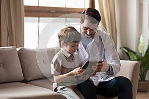 Friendly young pediatrician showing cartoons on tablet to little patient.