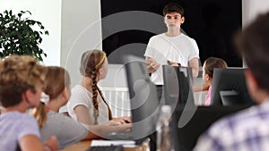Friendly young teacher standing near an interactive whiteboard telling new material to teenage students in a school