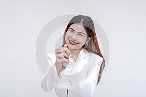 A friendly young woman smiling at the camera asking for a favor with hands clasped together. Isolated on a white background