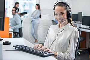 Friendly young woman working in call center office with team as the customer care operators.