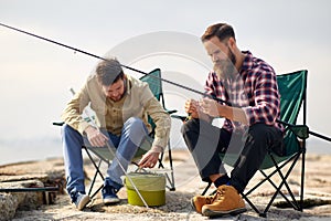 Friends adjusting fishing rods with bait on pier