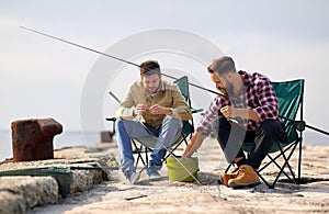 Friends adjusting fishing rods with bait on pier