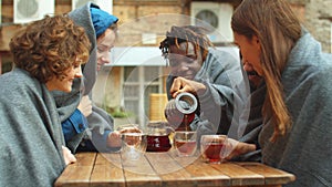 Friends in blankets sit outside the cafe and pour tea in cups