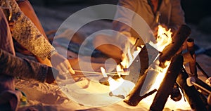 Friends, bonfire and roast marshmallows at night with beer, relax and bonding together for fun on beach. Men, women or