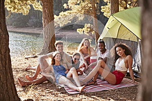 Friends camping out by a lake smiling to camera