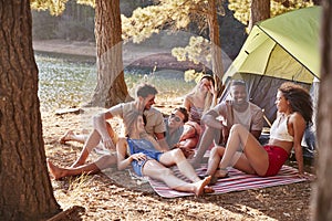 Friends on a camping trip relaxing on a blanket by a lake