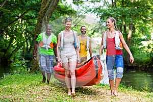 Friends carrying a canoe to river through forest