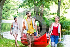 Friends carrying kayak or canoe to forest river