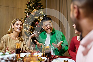 Friends celebrate Christmas eve or New Year holiday paty together sitting at the table. Feast at home group of multi