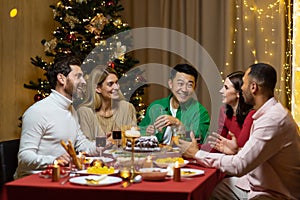 Friends celebrate Christmas eve or New Year holiday paty together sitting at the table. Feast at home group of multi