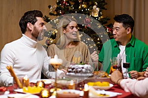 Friends celebrate Christmas eve or New Year holiday paty together sitting at the table. Feast at home group of multi