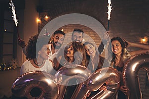 Friends celebrating New Years Eve waving with sparklers and holding 2020 balloons