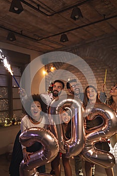 Friends celebrating New Years Eve waving with sparklers and holding 2021 balloons