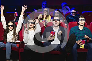 Friends in the cinema watch a funny movie with 3D glasses, laugh, have fun