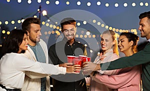 Friends clinking party cups on rooftop at night