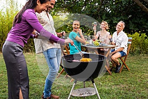 Friends cooking food on grill. Outdoor garden barbecue party. Friends laughing and having fun, enjoying wine in backyard