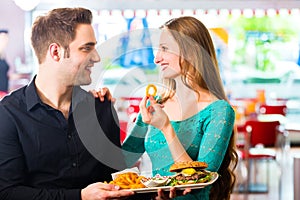 Friends or couple eating fast food with burger and fries